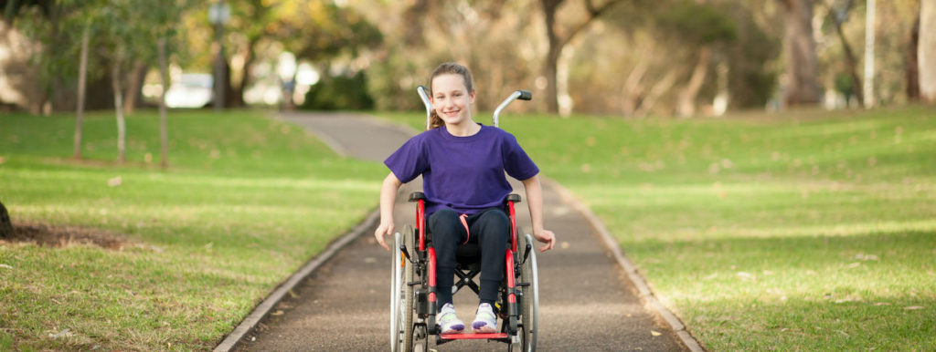 child in purple shirt in a red pediatric wheelchair