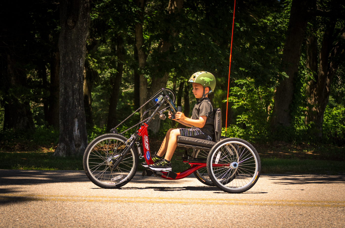 Young boy riding a red handcycle down a scenic path