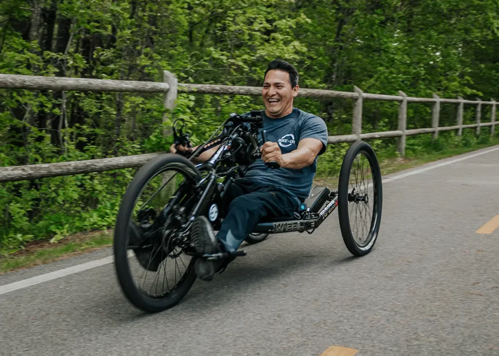 A man gleefully riding a Maddiline handcycle down an open road
