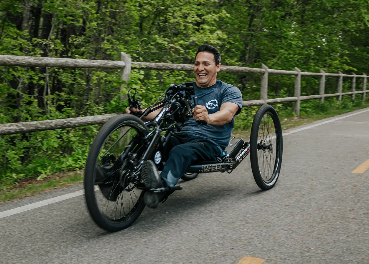 A man gleefully riding a Maddiline handcycle down an open road