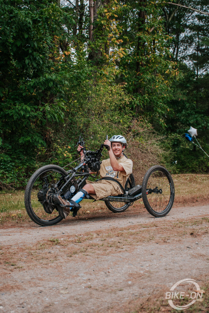 Teenage boy riding a Maddiline handcycle on a forest trail