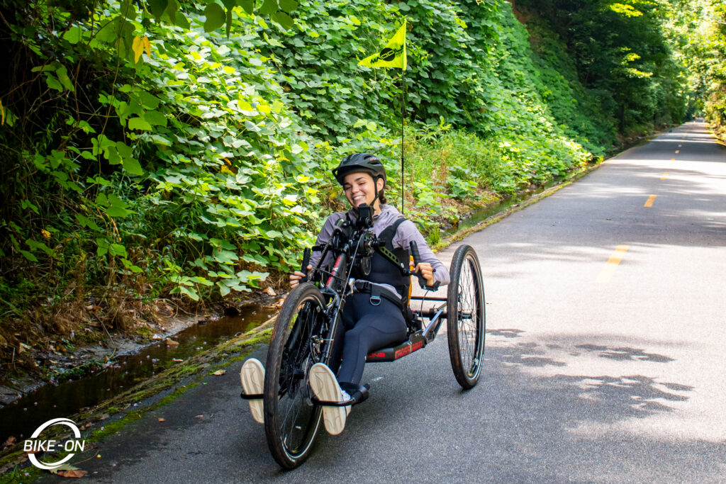 Girl smiling, sitting on a handcycle surrounded by trees